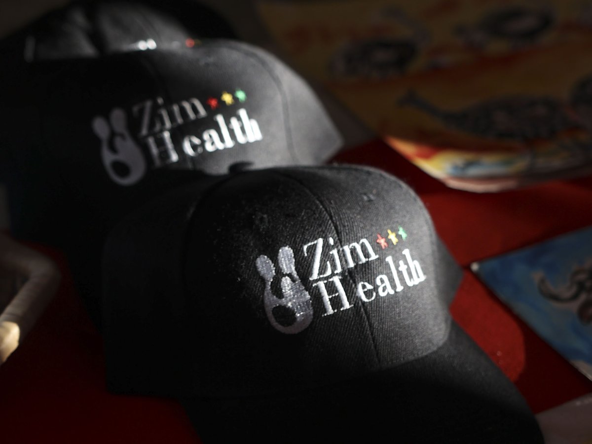 Embroidered Zimhealth caps beside children's paintings